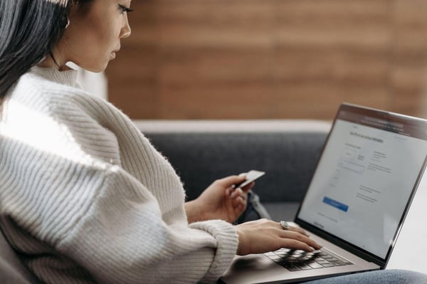 Woman in a white sweater entering card details into a laptop